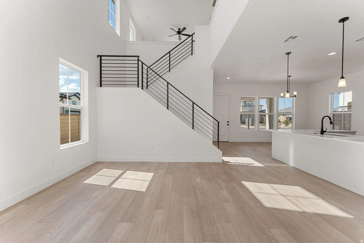 Unfurnished living room featuring plenty of natural light, hanging lights, light wood-style floors, a high ceiling, and a ceiling fan
