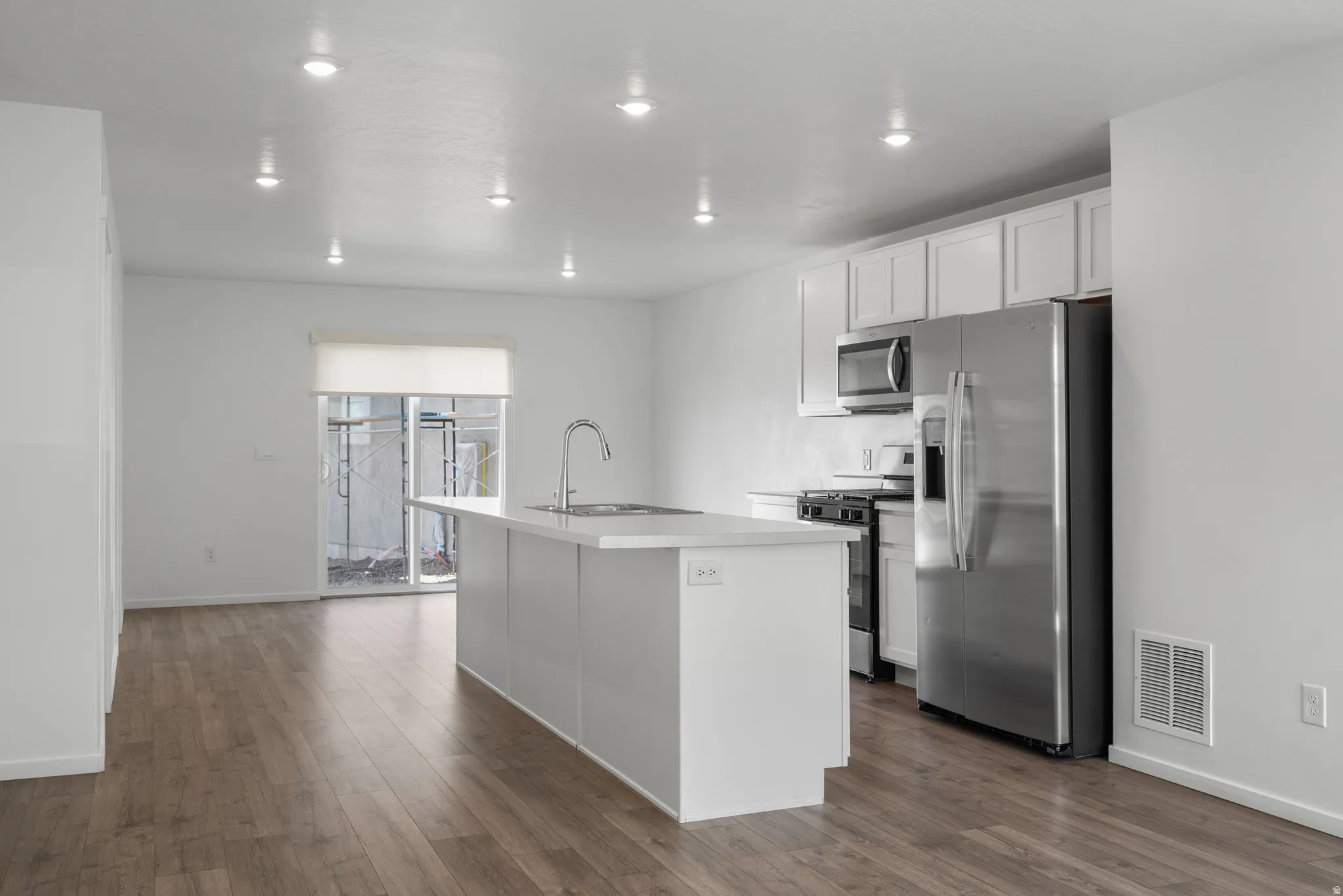 Kitchen with stainless steel appliances, white cabinets, dark wood finished floors, a kitchen island with sink, and light countertops