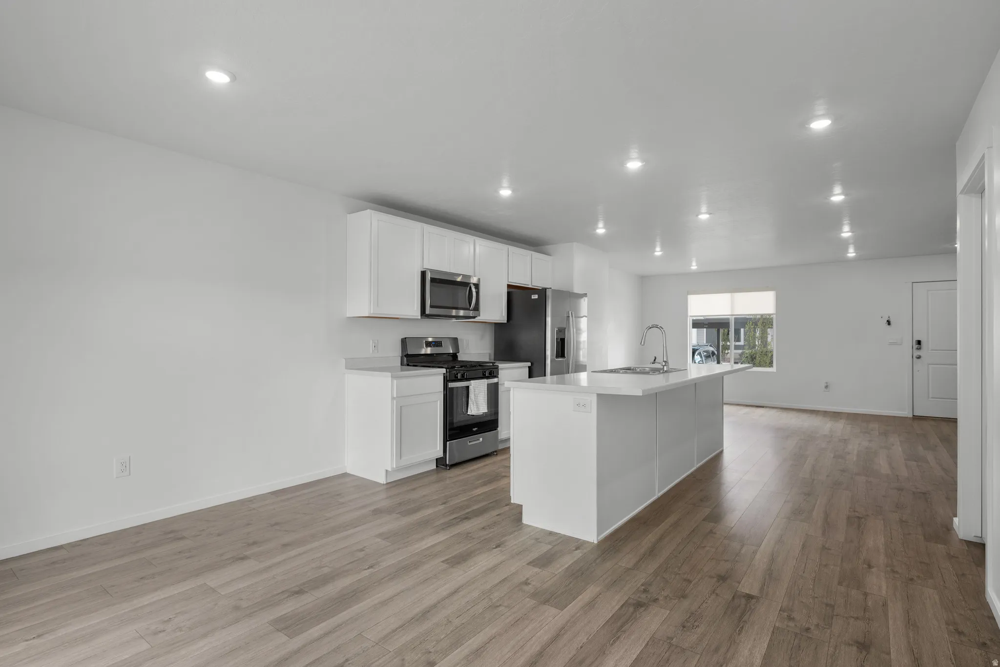 Kitchen featuring stainless steel appliances, white cabinetry, an island with sink, light wood finished floors, and recessed lighting