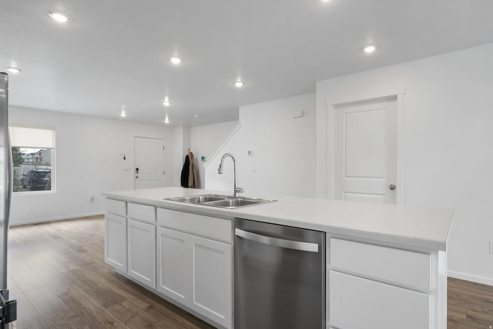 Kitchen featuring stainless steel dishwasher, light countertops, an island with sink, dark wood-style floors, and white cabinetry