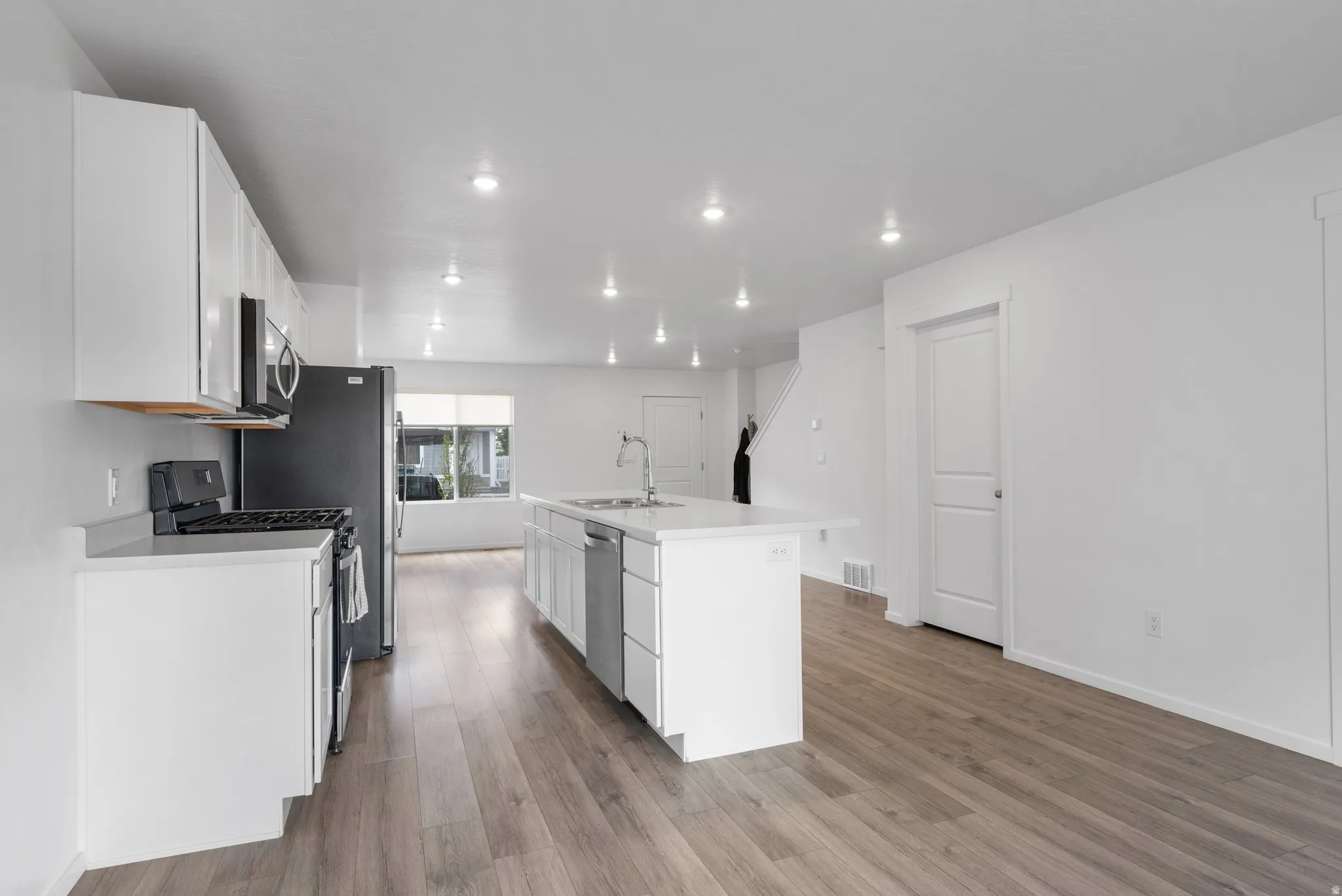 Kitchen featuring white cabinets, a kitchen island with sink, stainless steel appliances, light wood-style flooring, and recessed lighting