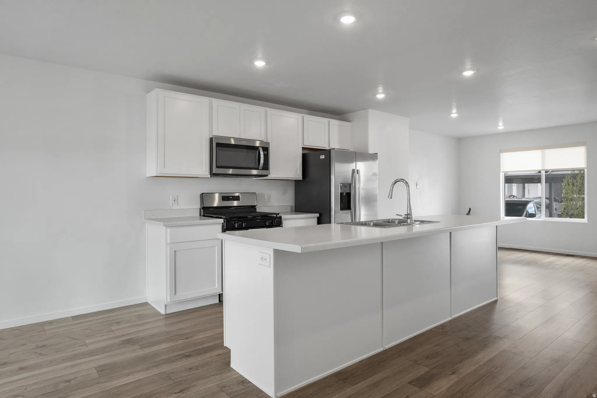 Kitchen with light countertops, stainless steel appliances, white cabinets, a center island with sink, and dark wood-style flooring