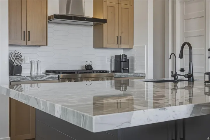 Kitchen featuring light stone countertops, decorative backsplash, and stainless steel range with gas stovetop