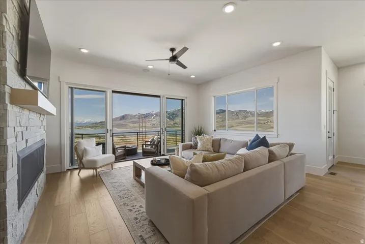 Living area featuring a stone fireplace, light wood-type flooring, a ceiling fan, and recessed lighting