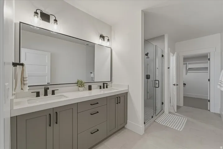 Full bath featuring double vanity, a stall shower, a spacious closet, and light tile patterned floors