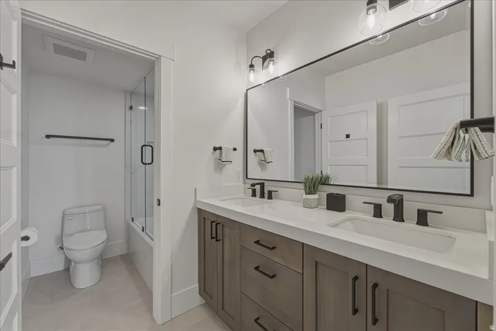 Bathroom featuring double vanity, shower / bath combination with glass door, and light tile patterned flooring