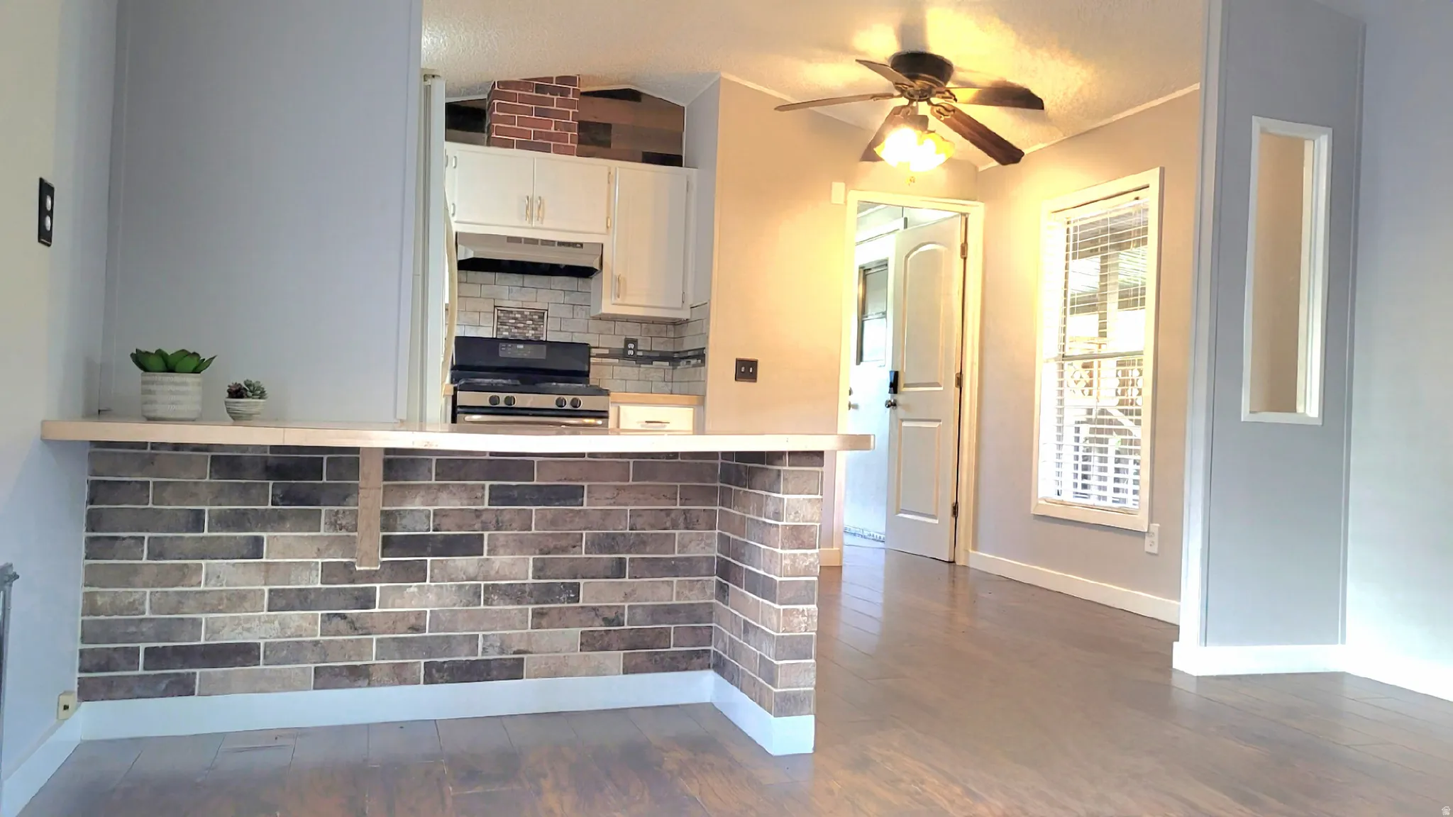 Kitchen with decorative backsplash, black stove, ceiling fan, light countertops, and white cabinetry
