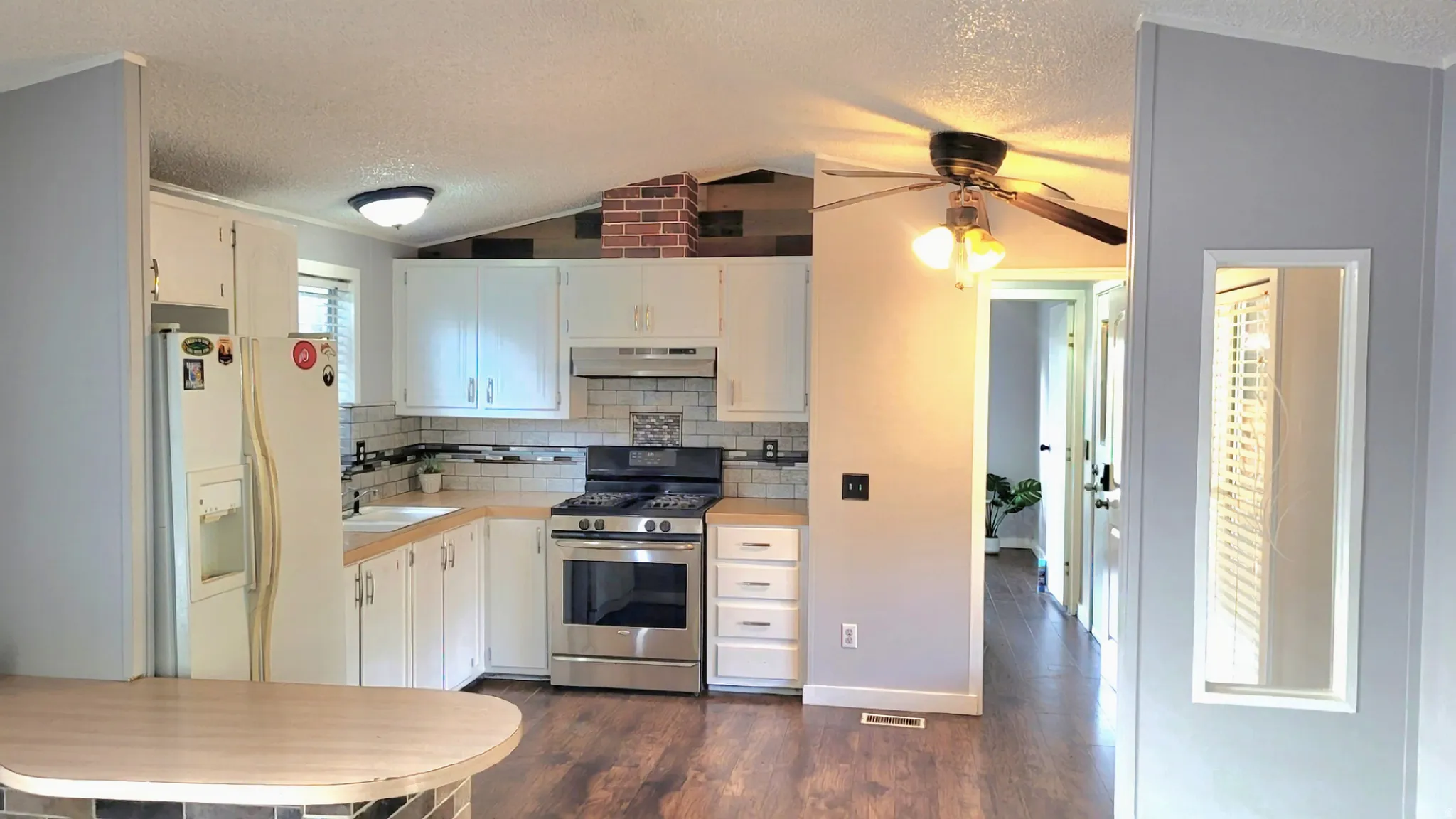 Kitchen with white refrigerator with ice dispenser, gas stove, white cabinets, dark wood-type flooring, and decorative backsplash