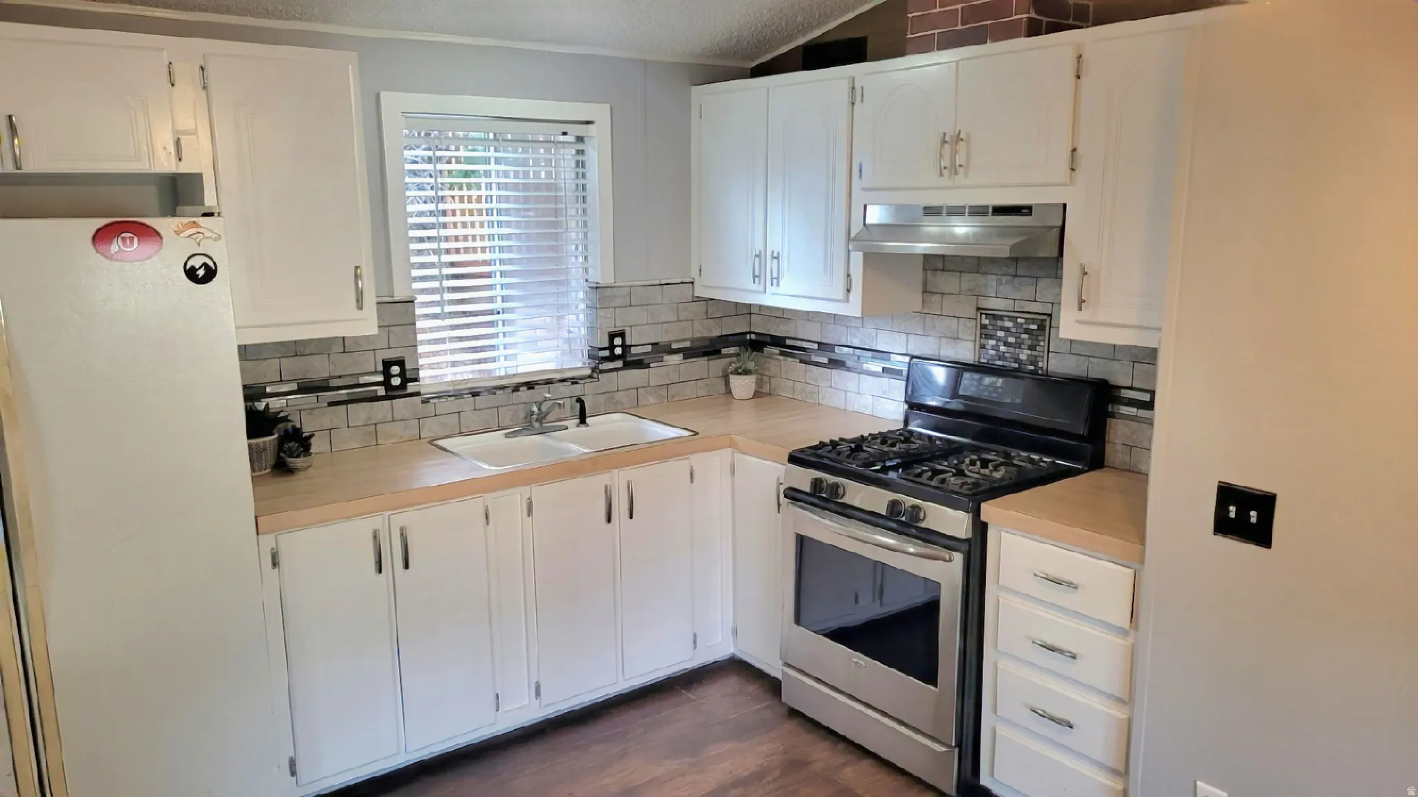 Kitchen featuring gas range, freestanding refrigerator, light countertops, white cabinetry, and ventilation hood