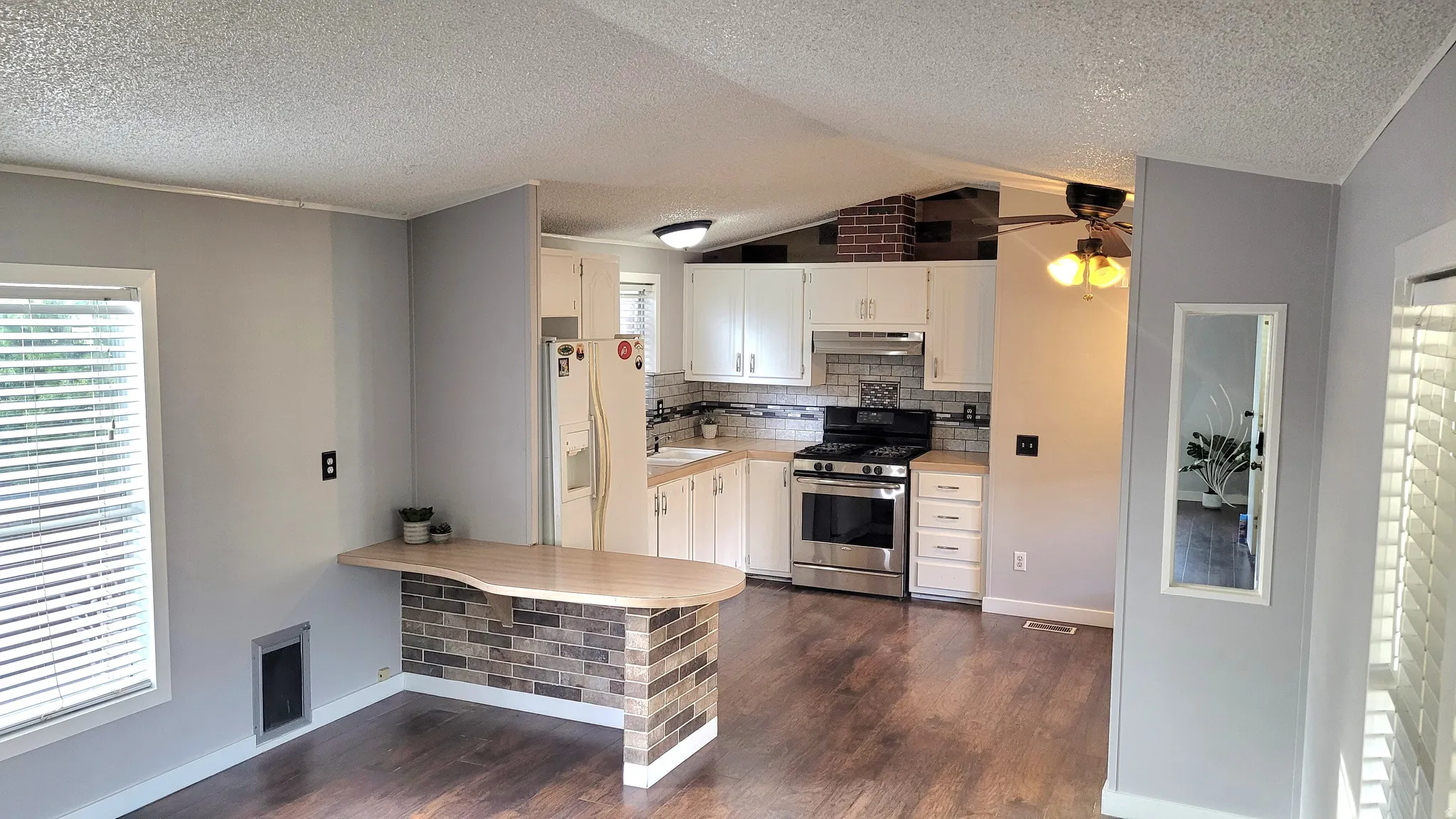 Kitchen featuring light countertops, white cabinetry, stainless steel range with gas cooktop, a textured ceiling, and white refrigerator with ice dispenser