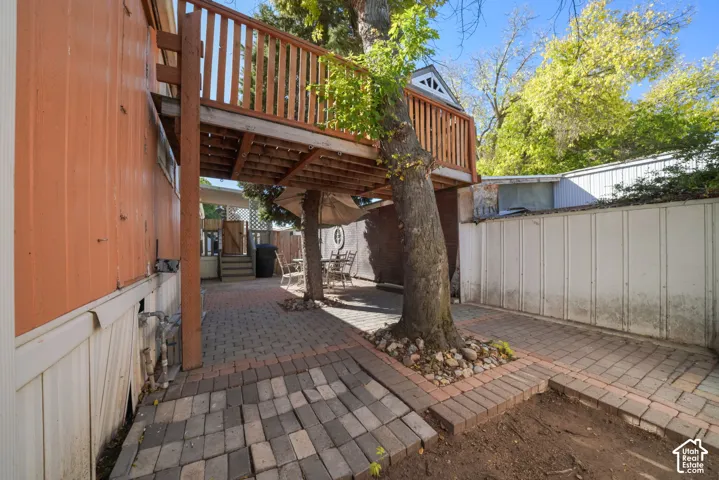 Outdoor patio featuring paver hardscaping, an elevated wood deck, and mature trees with stone landscaping borders