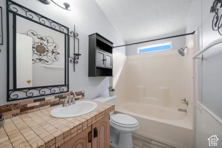 Tiled countertop with integrated vanity sink, wood-finish cabinetry, built-in storage cabinet, and a combination tub and shower surround