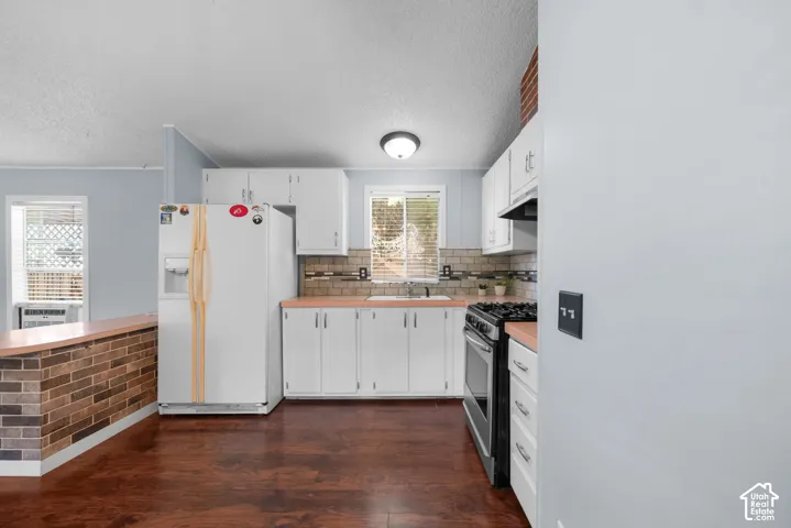 Kitchen featuring white cabinetry, wood-finish flooring, brick-accented peninsula, and tile backsplash