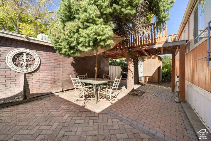Herringbone-patterned brick paver patio featuring a raised wooden deck platform and decorative brick wall masonry