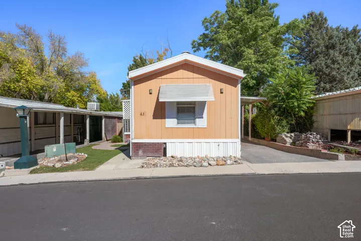 Exterior facade featuring vertical siding, a window awning, and a paved driveway with a covered parking area