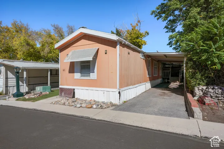 Single-level exterior featuring light-toned vertical siding, an attached covered carport, and a gravel landscape bed