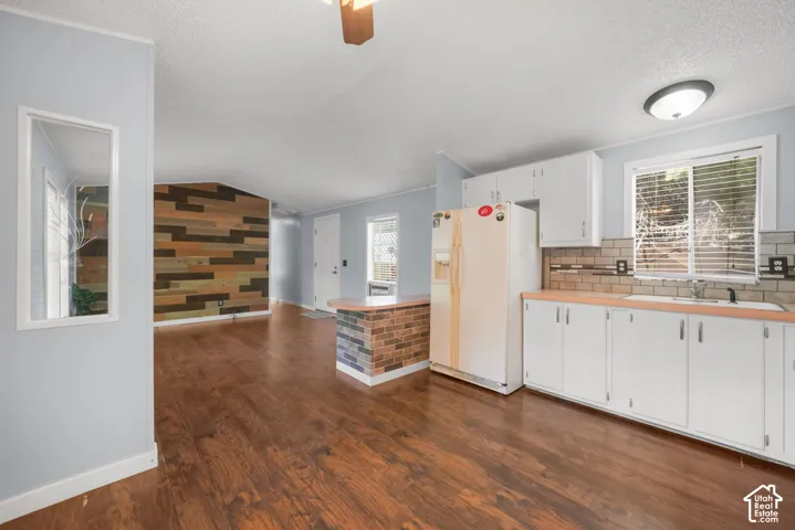 Kitchen featuring white cabinetry, wood-finish flooring, brick-accented peninsula, and a horizontal wood-plank decorative wall