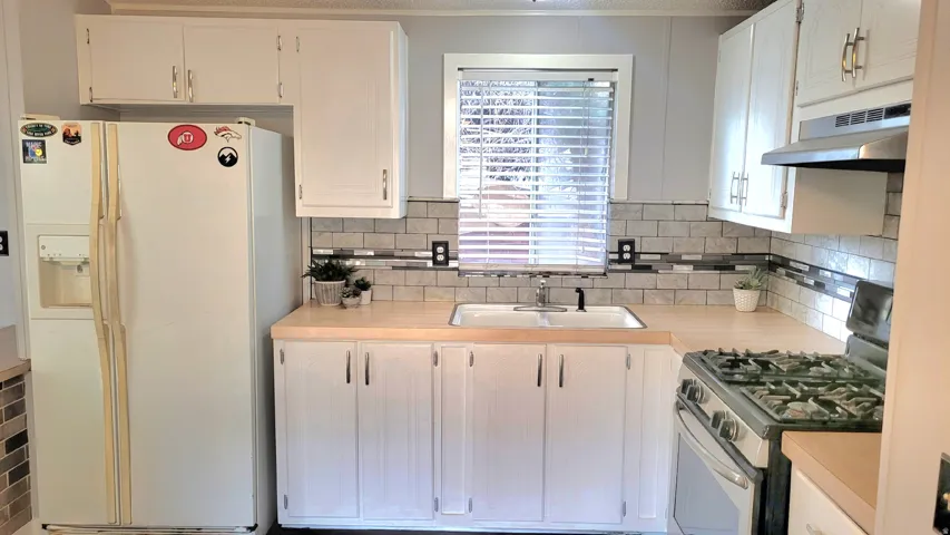 Kitchen with stainless steel gas range oven, white refrigerator with ice dispenser, light countertops, and white cabinets