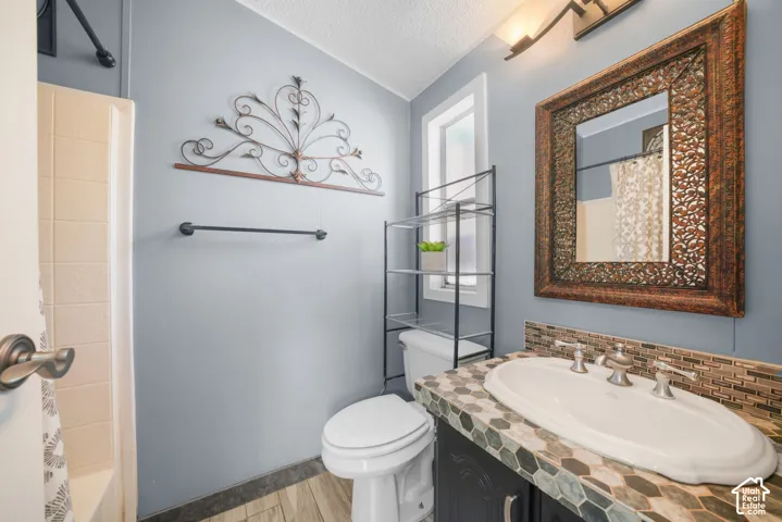 Vanity featuring a patterned tile countertop, drop-in sink, and multi-tone horizontal stone backsplash, wood-finish flooring, and shower enclosure with tile surround