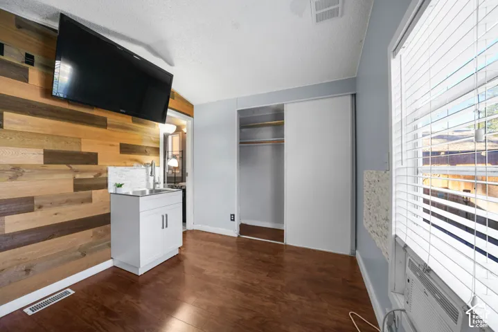 Multi-tonal wood-plank accent wall featuring an integrated vanity with a stainless steel sink and white cabinetry, wood-finish flooring, and a built-in closet with sliding doors