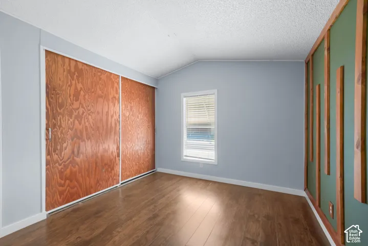 Interior room featuring wood-finish flooring, sliding wood-panel closet doors, and decorative wall paneling with vertical wood trim