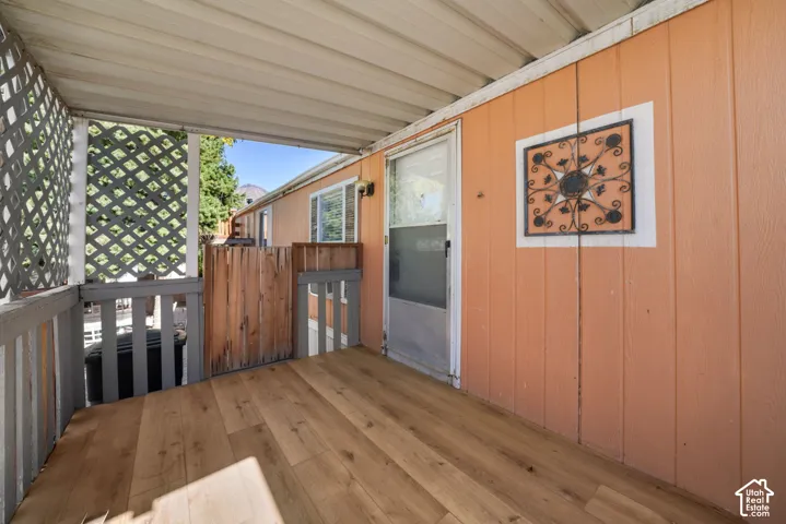 Covered porch featuring wood-finish flooring, vertical panel siding, and decorative lattice screen walling