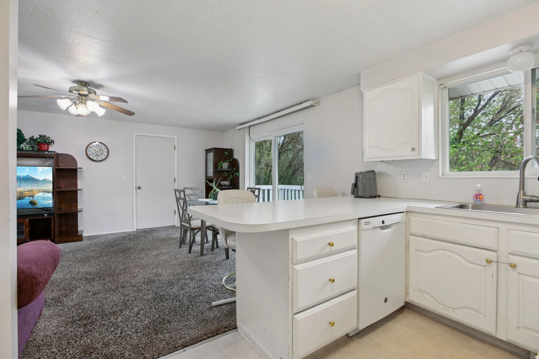 Kitchen featuring light countertops, a peninsula, white cabinets, white dishwasher, and a kitchen breakfast bar