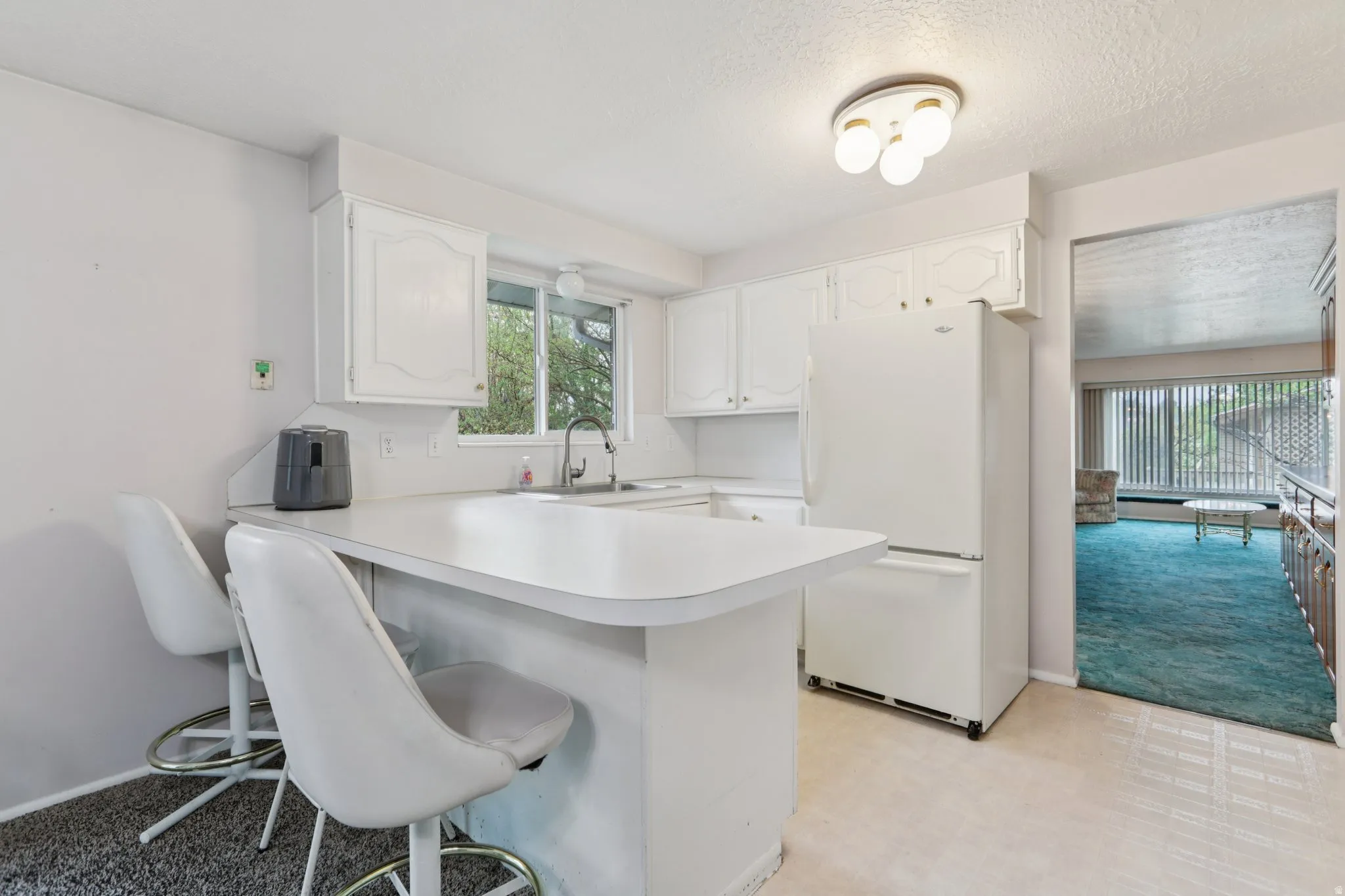 Kitchen with a kitchen bar, freestanding refrigerator, white cabinetry, light countertops, and a peninsula