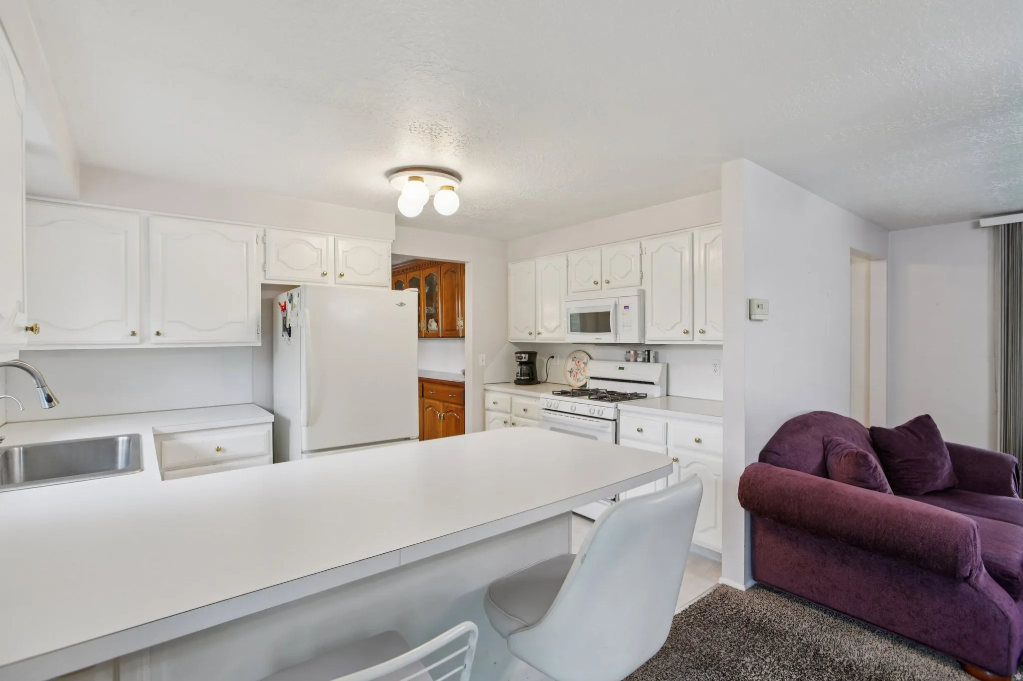 Kitchen with a kitchen breakfast bar, white cabinetry, white appliances, a peninsula, and a textured ceiling