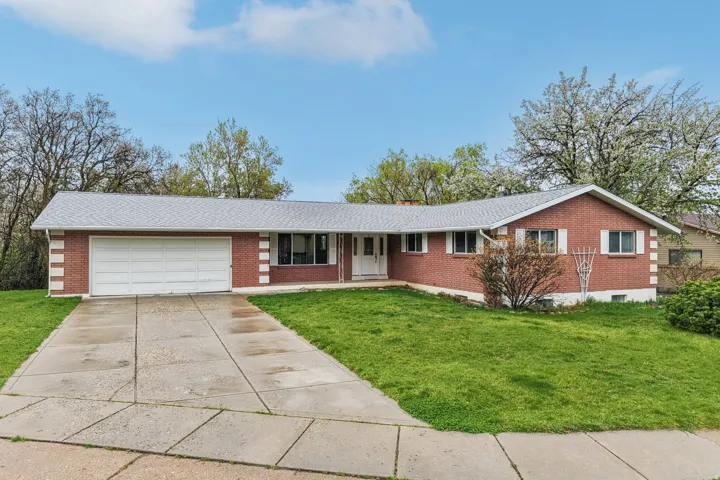 Ranch-style house with a front yard, concrete driveway, brick siding, and an attached garage