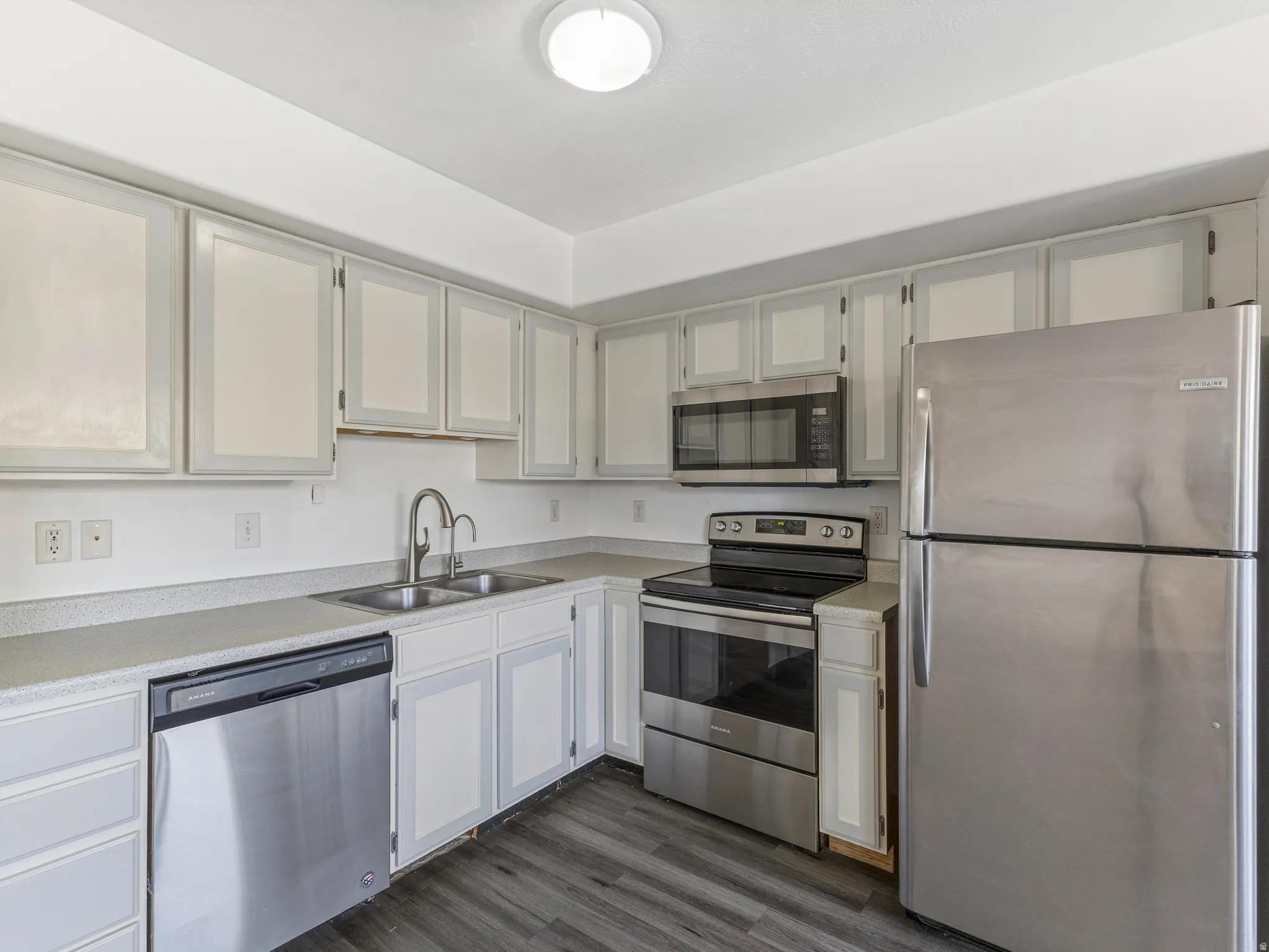 Kitchen featuring stainless steel appliances, light countertops, dark wood-style floors, and white cabinets