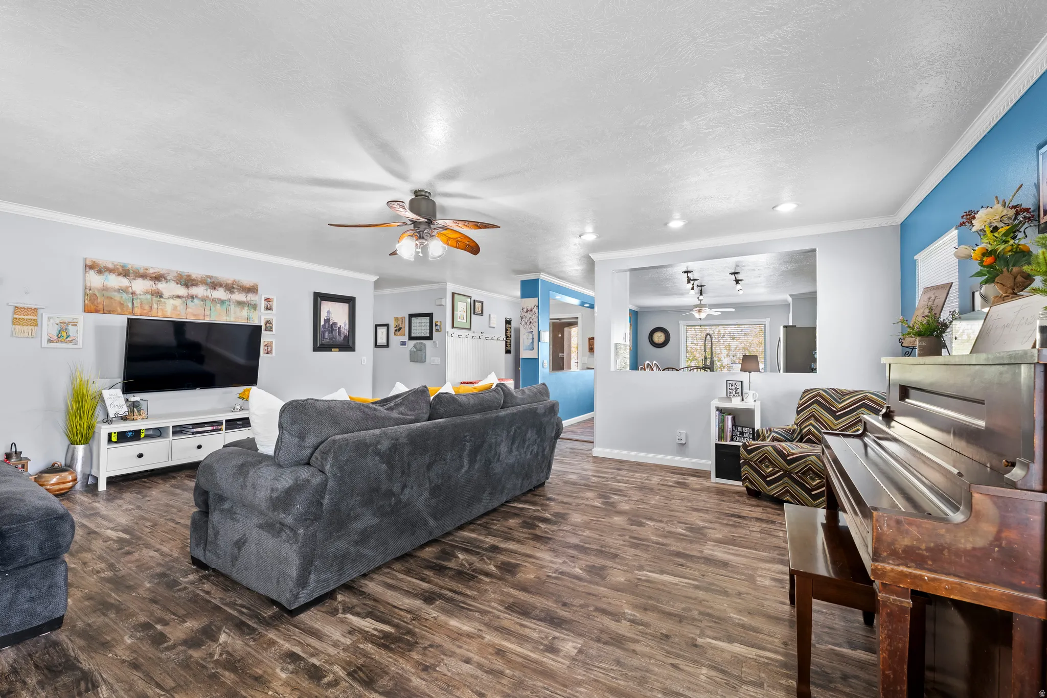 Living area featuring ornamental molding, a textured ceiling, dark wood-type flooring, and a ceiling fan