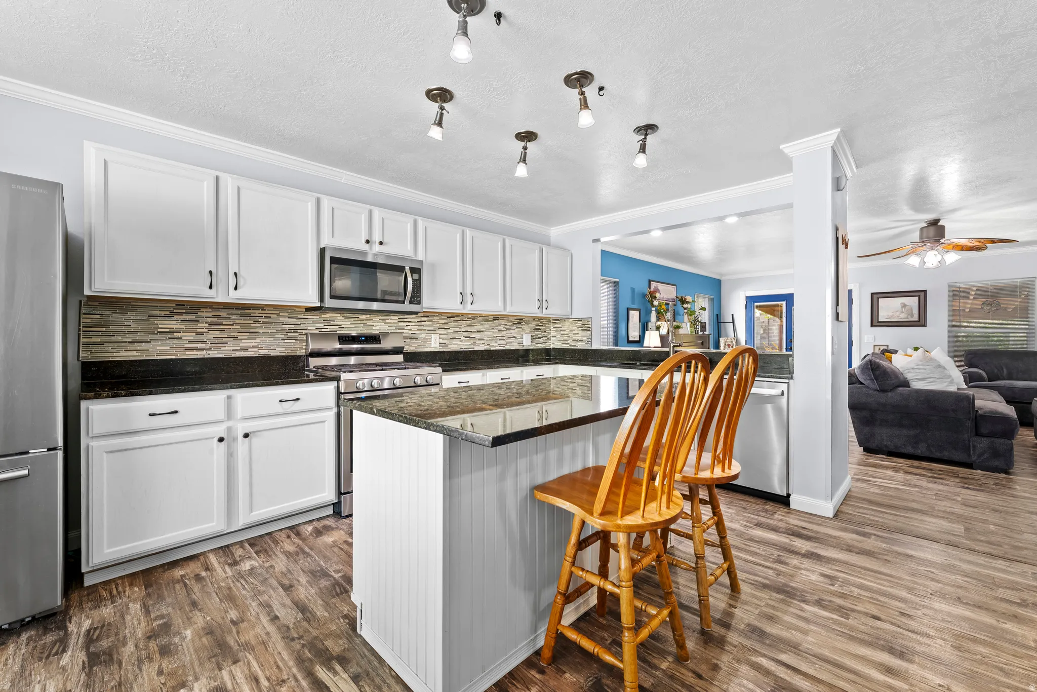 Kitchen featuring a kitchen breakfast bar, dark stone counters, stainless steel appliances, LVP flooring and white cabinets.