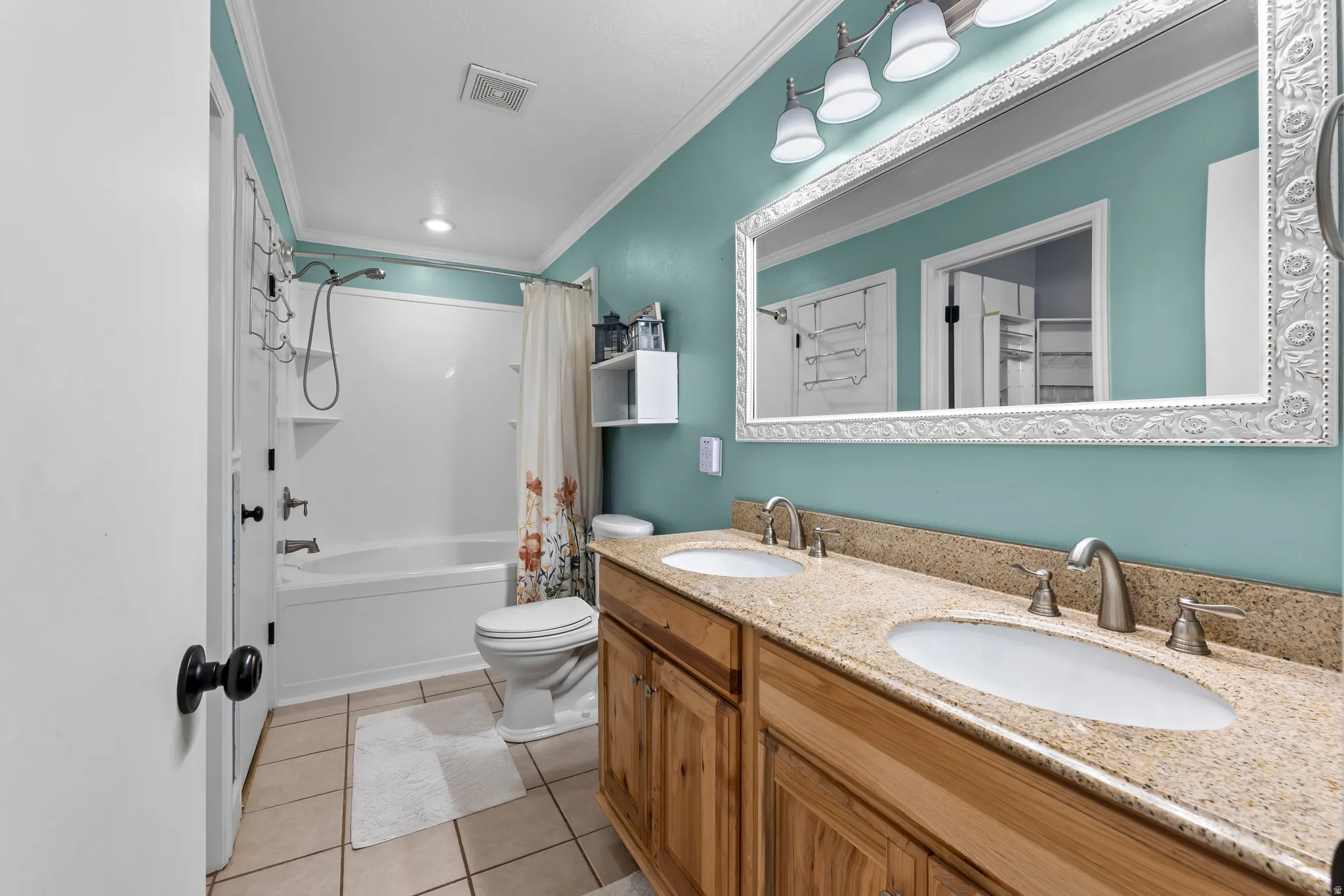 Primary bath en suite with double vanity, crown molding, light tile and oversized shower/tub.