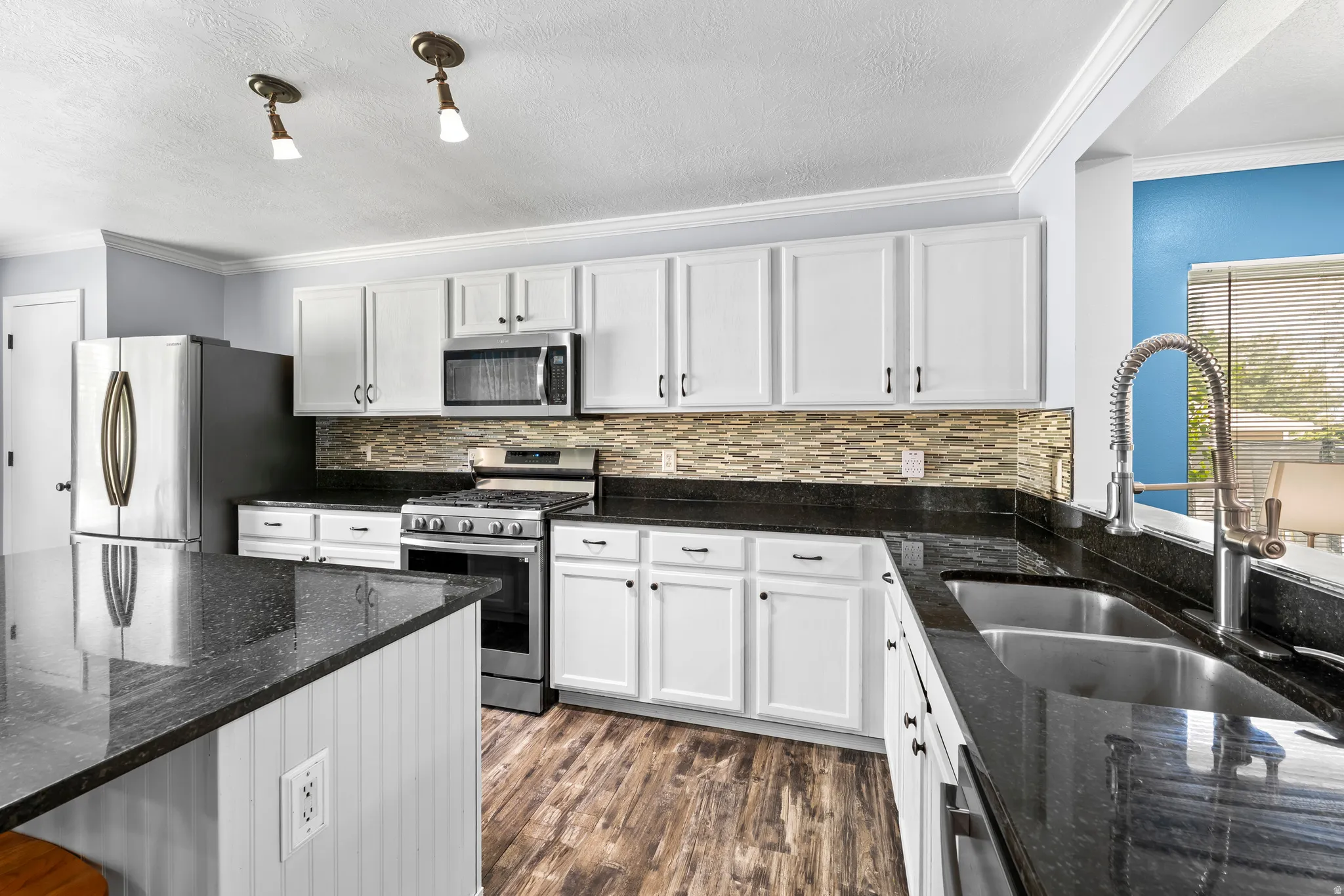 Kitchen with granite countertop, stainless steel appliances, white cabinetry, LVP flooring, and crown molding