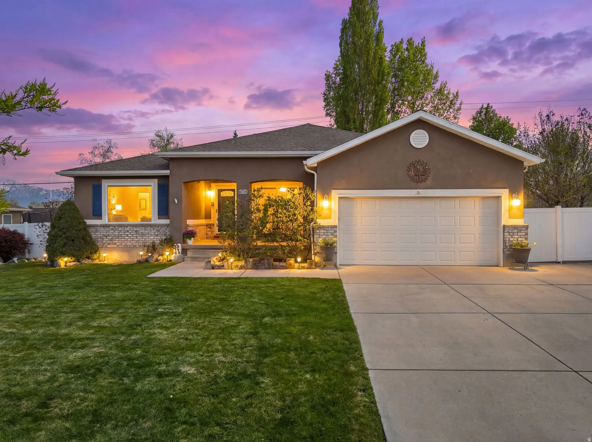 Rambler home with a 2- car garage + RV pad, a cute front porch, stucco and brick exterior, and ample parking in the driveway.