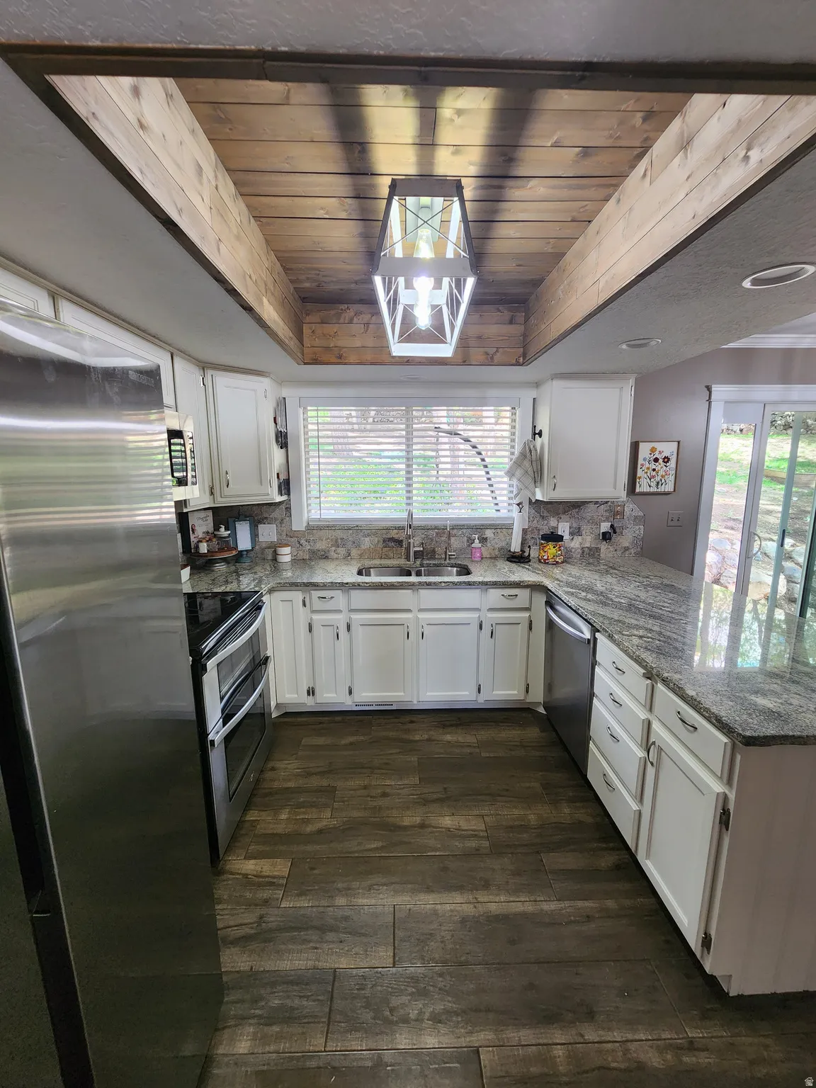 Kitchen featuring a wooden tray ceiling, white cabinetry, stainless steel appliances, light stone counters, and dark wood-style floors