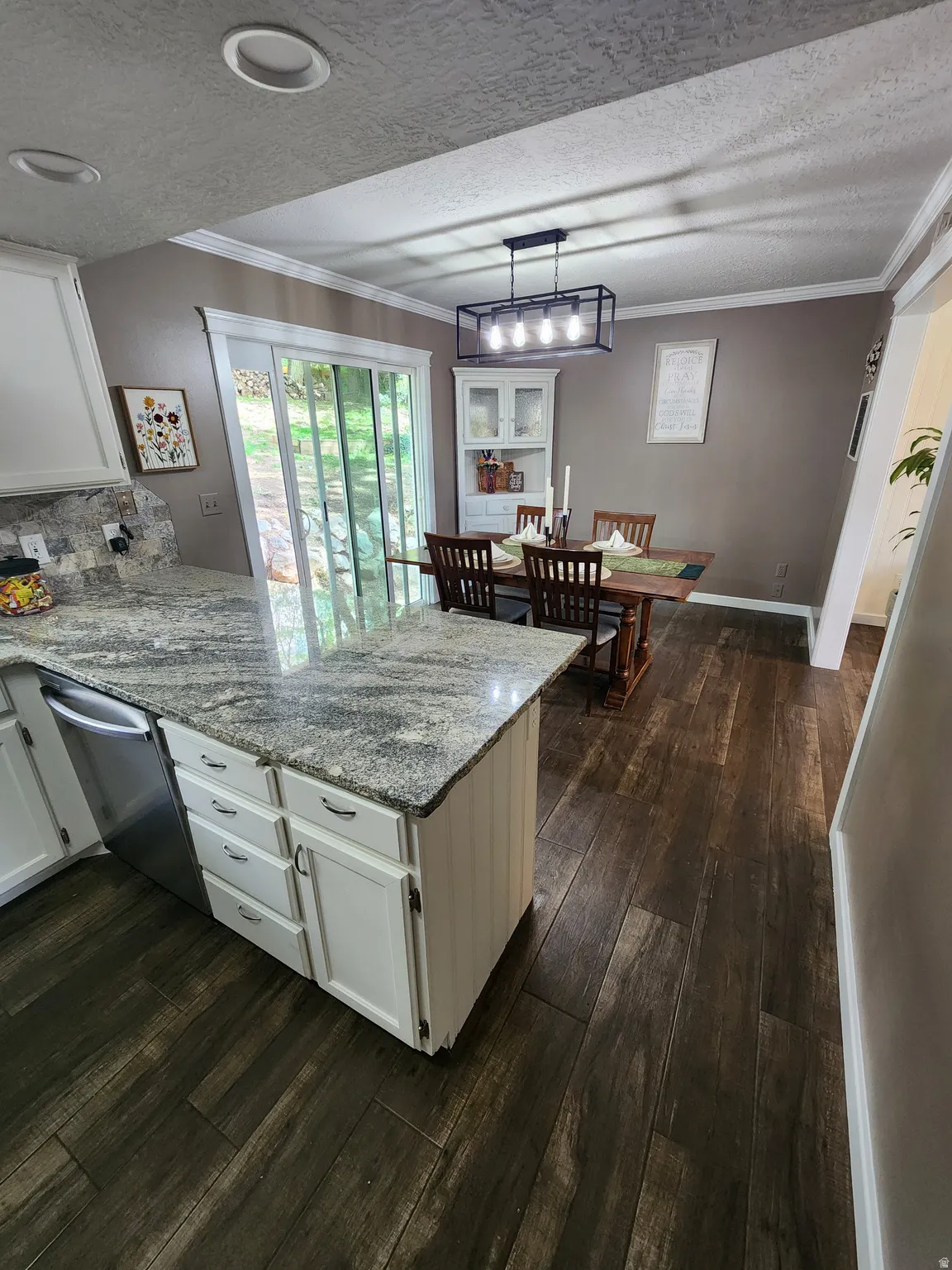 Kitchen with a peninsula, white cabinets, light stone counters, dark wood-style floors, and crown molding
