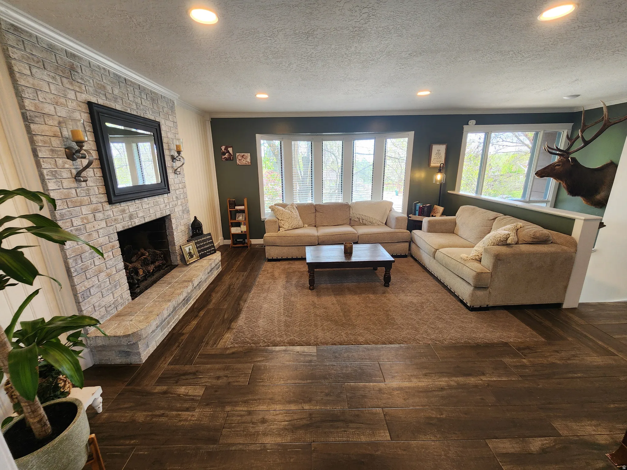 Living area with dark wood-style flooring, a brick fireplace, recessed lighting, healthy amount of natural light, and a textured ceiling