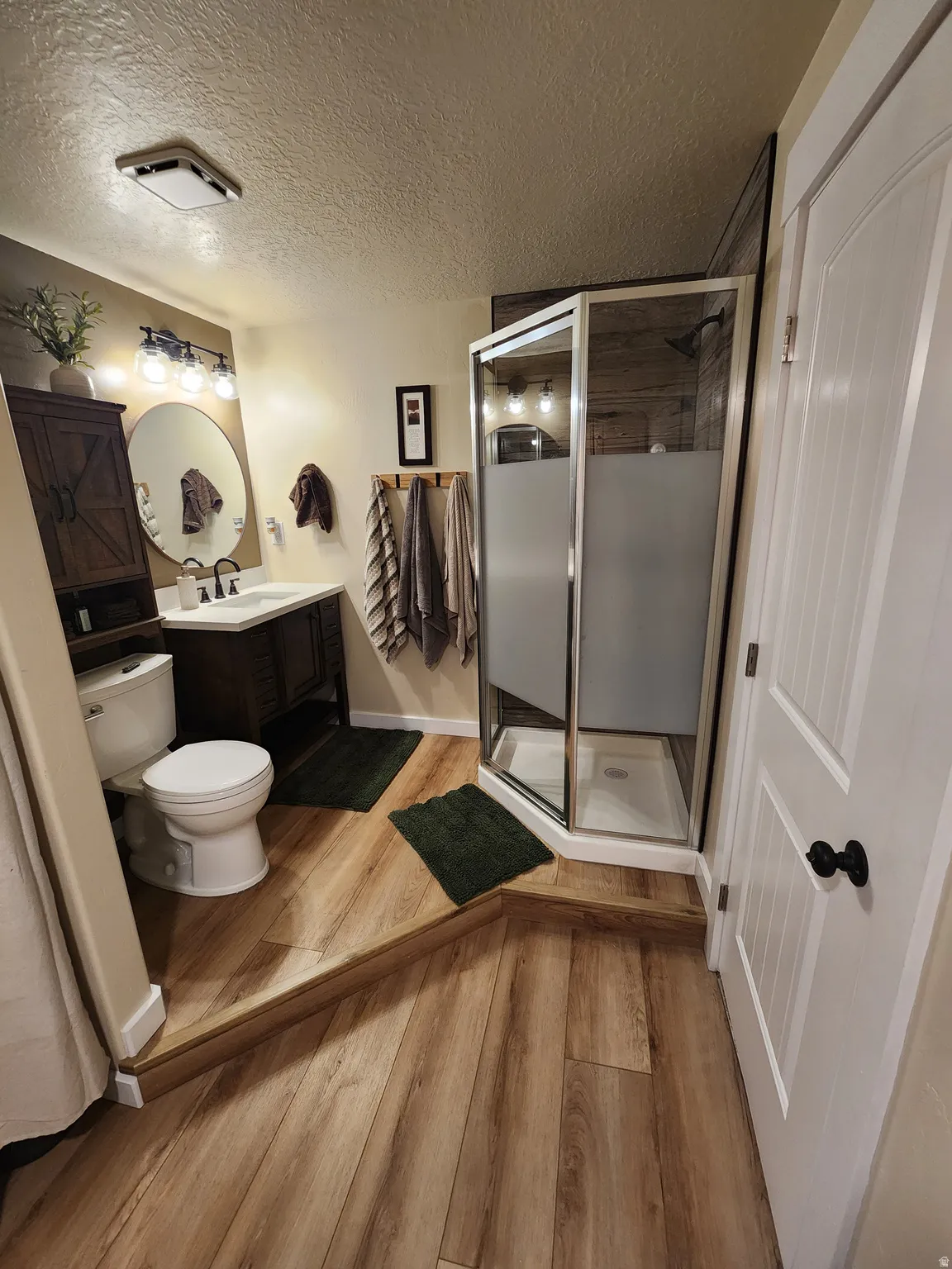 Bathroom with vanity, a stall shower, light wood-style flooring, and a textured ceiling