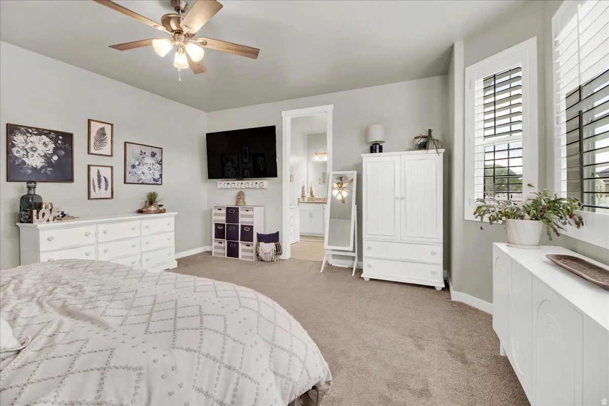 Bedroom with light carpet, ceiling fan, and ensuite bath