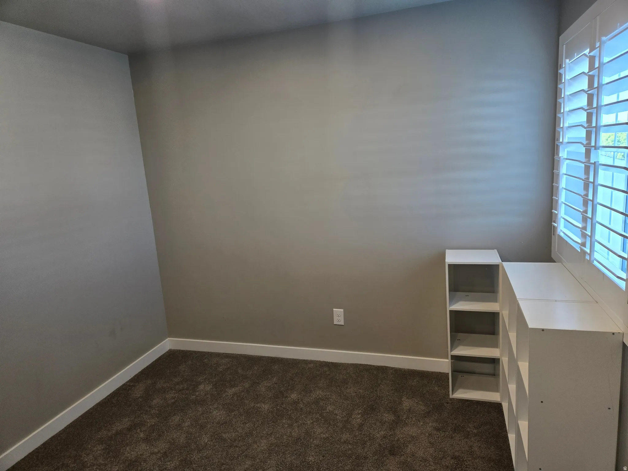 Room featuring plush carpet, neutral wall paint, white baseboards, and a window with white plantation shutters