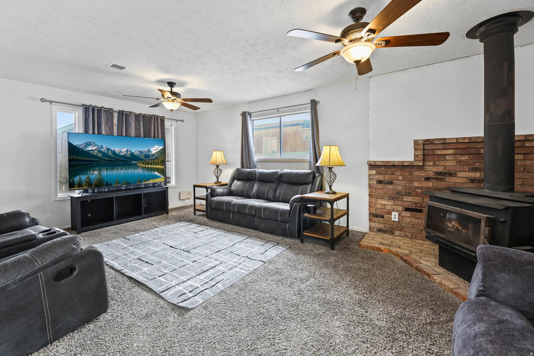 Living area featuring ceiling fan, carpet, a textured ceiling, and a wood stove