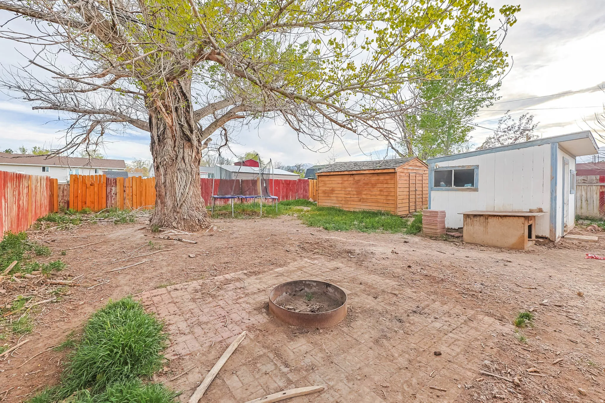 Fenced backyard with a trampoline, a shed, a fire pit, and a patio area