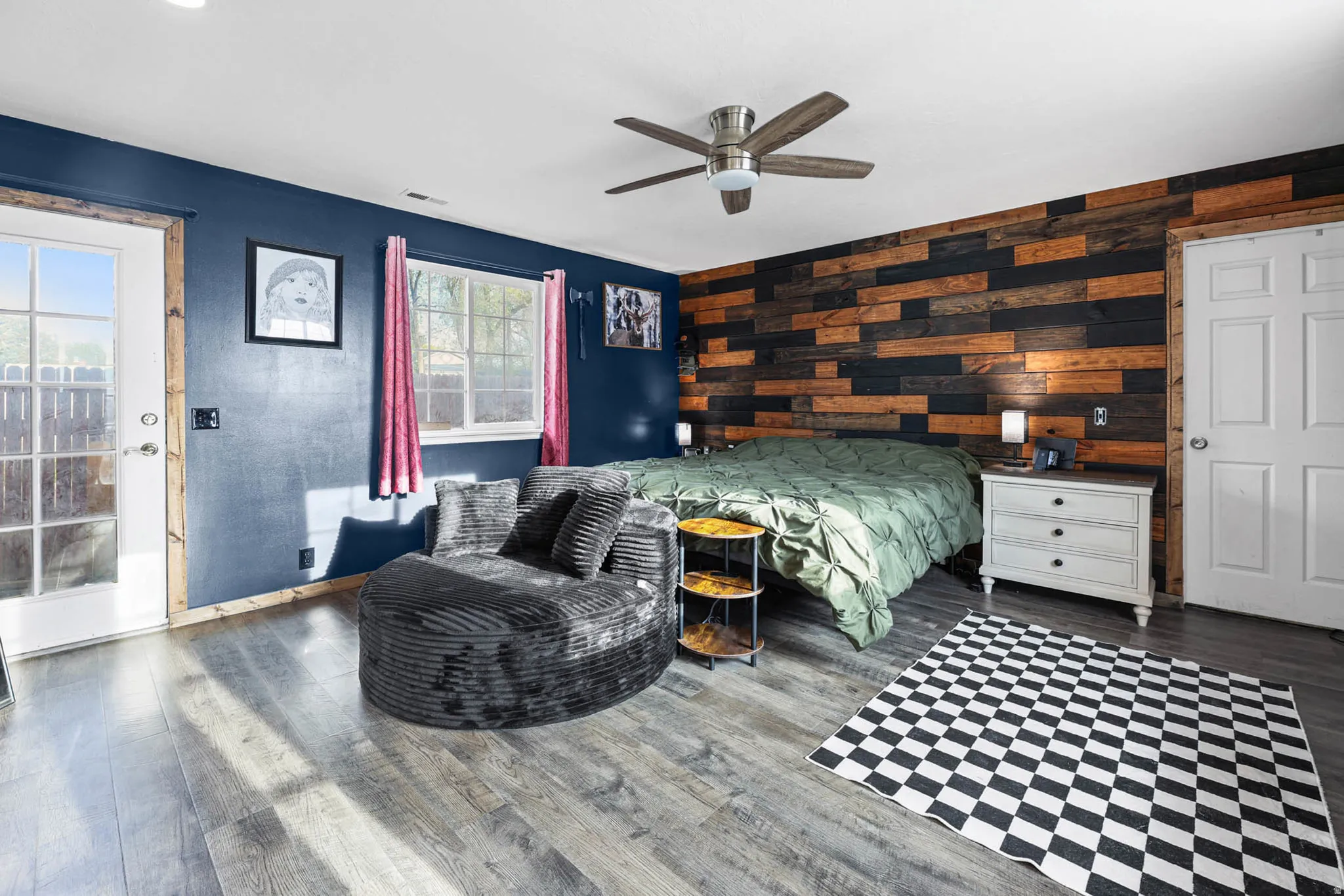 Bedroom featuring wood finished floors, wooden walls, a ceiling fan, and an accent wall