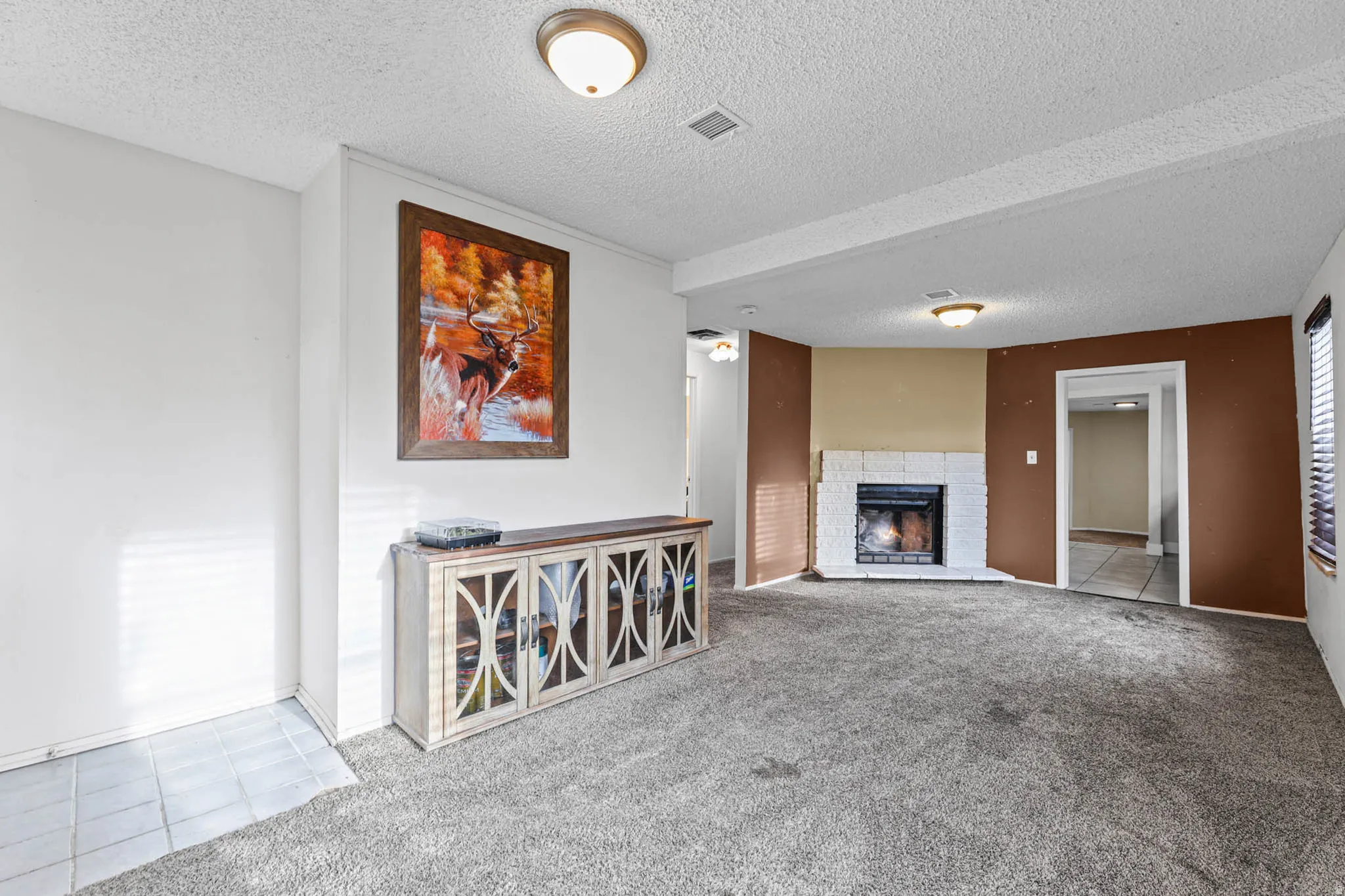 Unfurnished living room with light colored carpet, a textured ceiling, light tile patterned flooring, and a fireplace