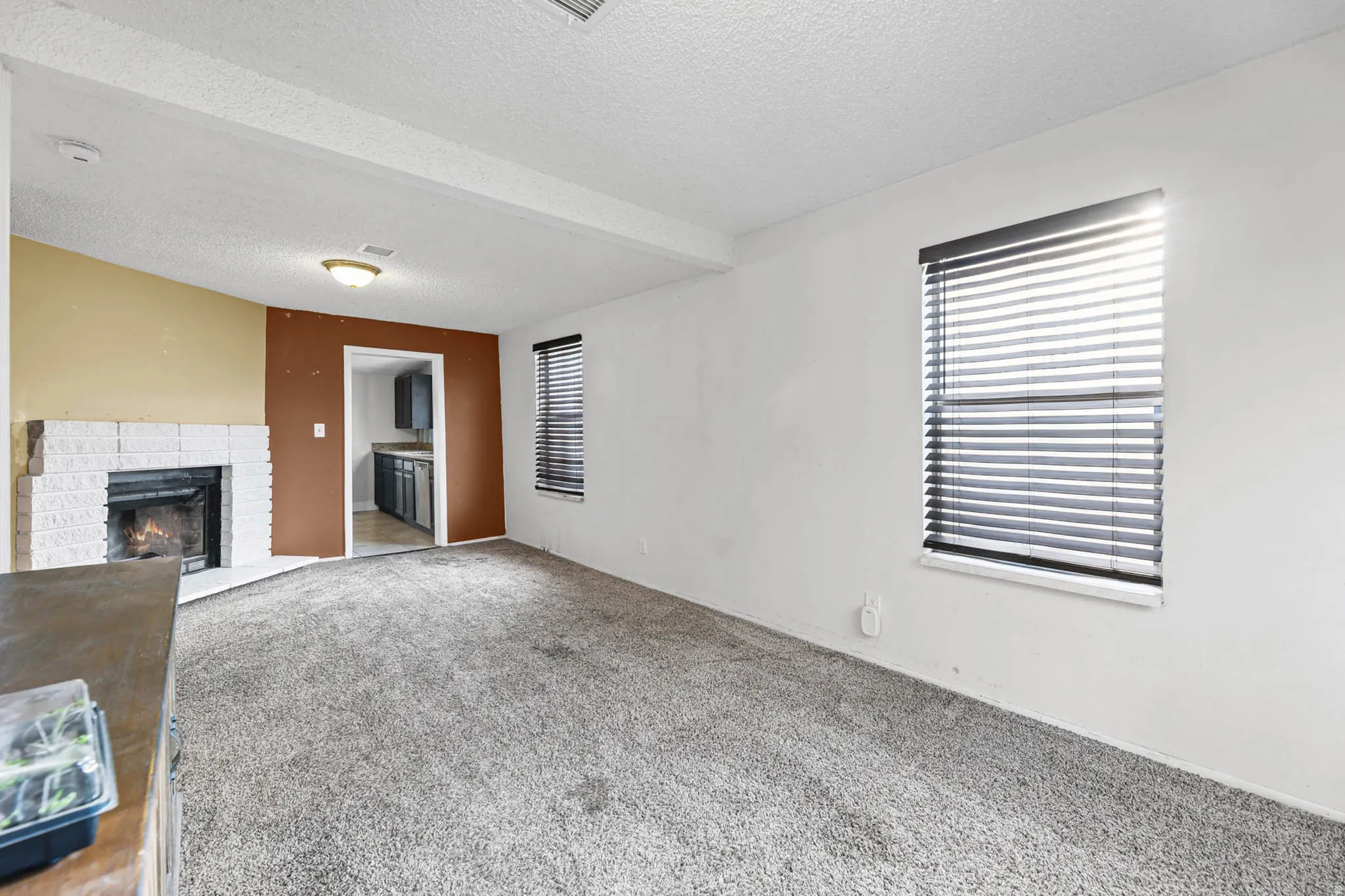 Unfurnished living room with a textured ceiling, carpet flooring, and a brick fireplace
