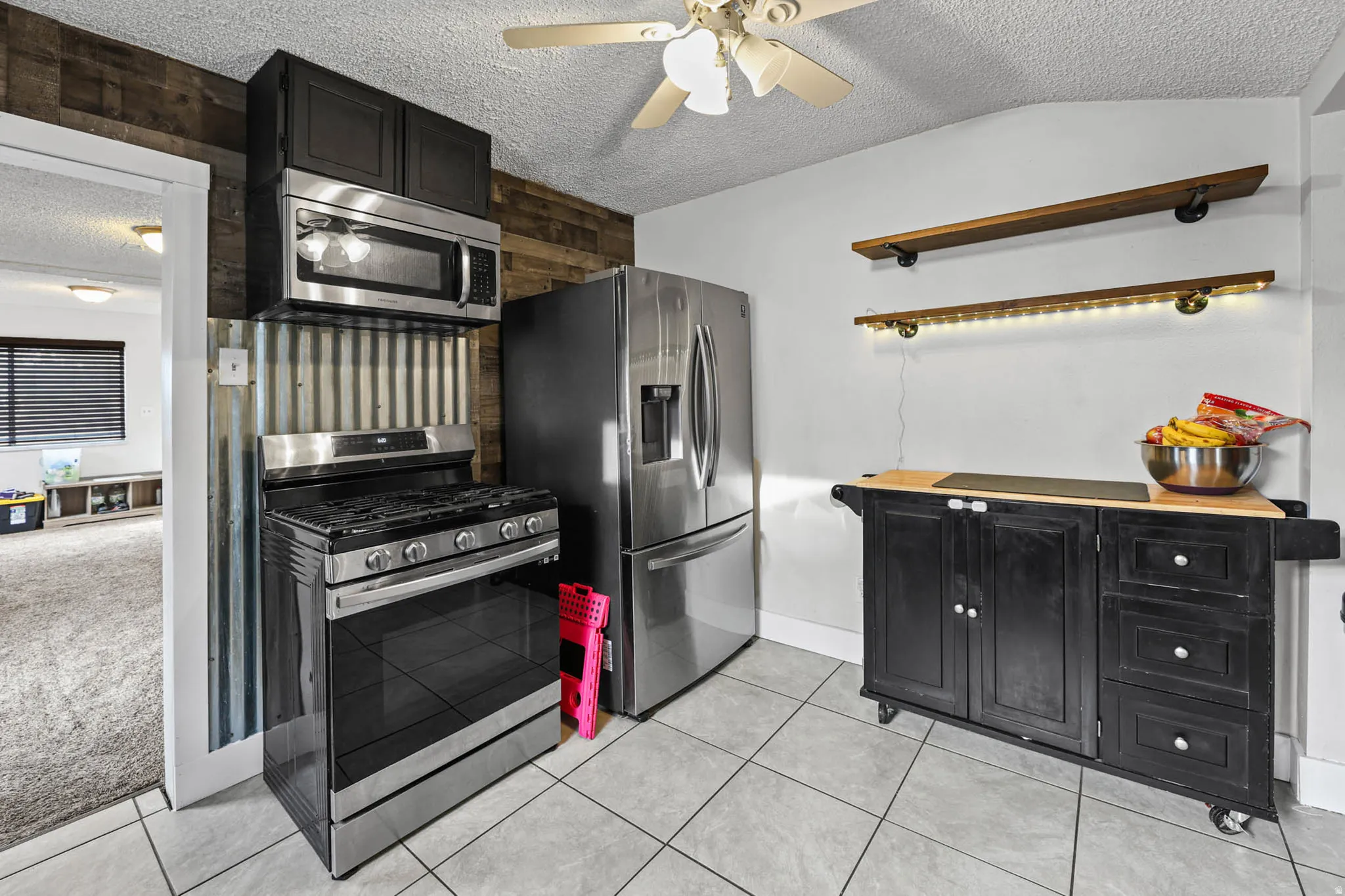 Kitchen with dark cabinets, a textured ceiling, stainless steel appliances, a ceiling fan, and open shelves