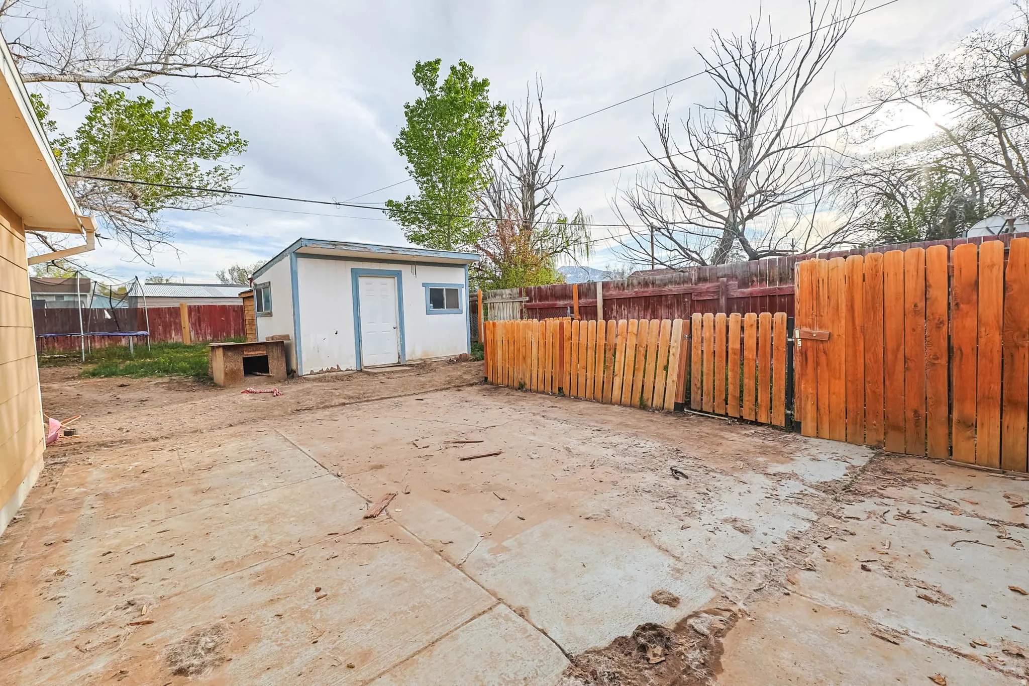 Fenced backyard with an outbuilding, a patio area, a trampoline, and a gate