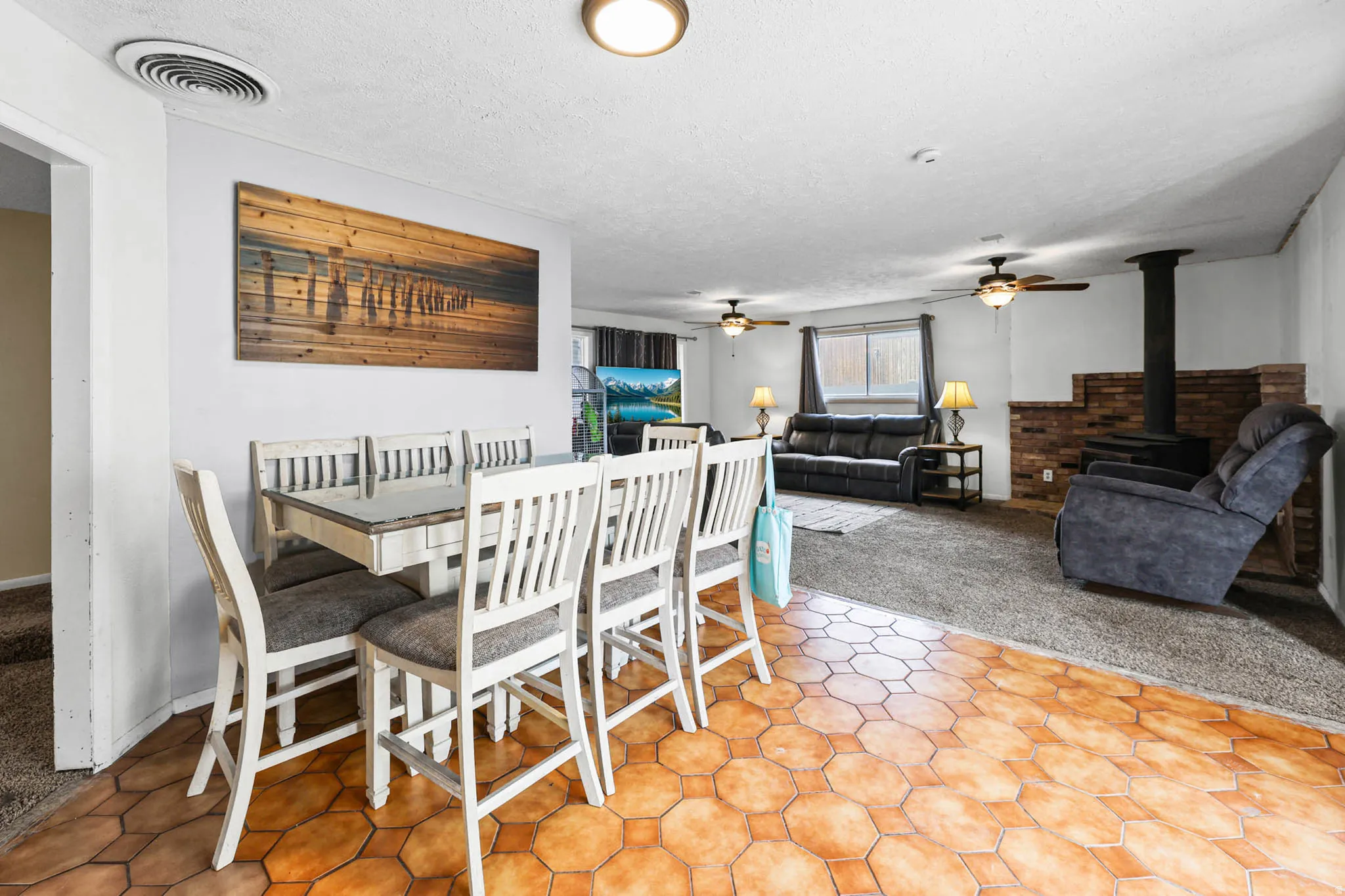 Dining room with a wood stove, ceiling fan, light carpet, and a textured ceiling
